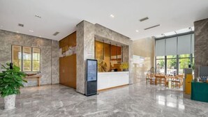 Ein moderner Empfangsbereich mit Marmorboden, einer Rezeption, einer digitalen Infotafel und einer Sitzecke mit Stühlen und einem Tisch.