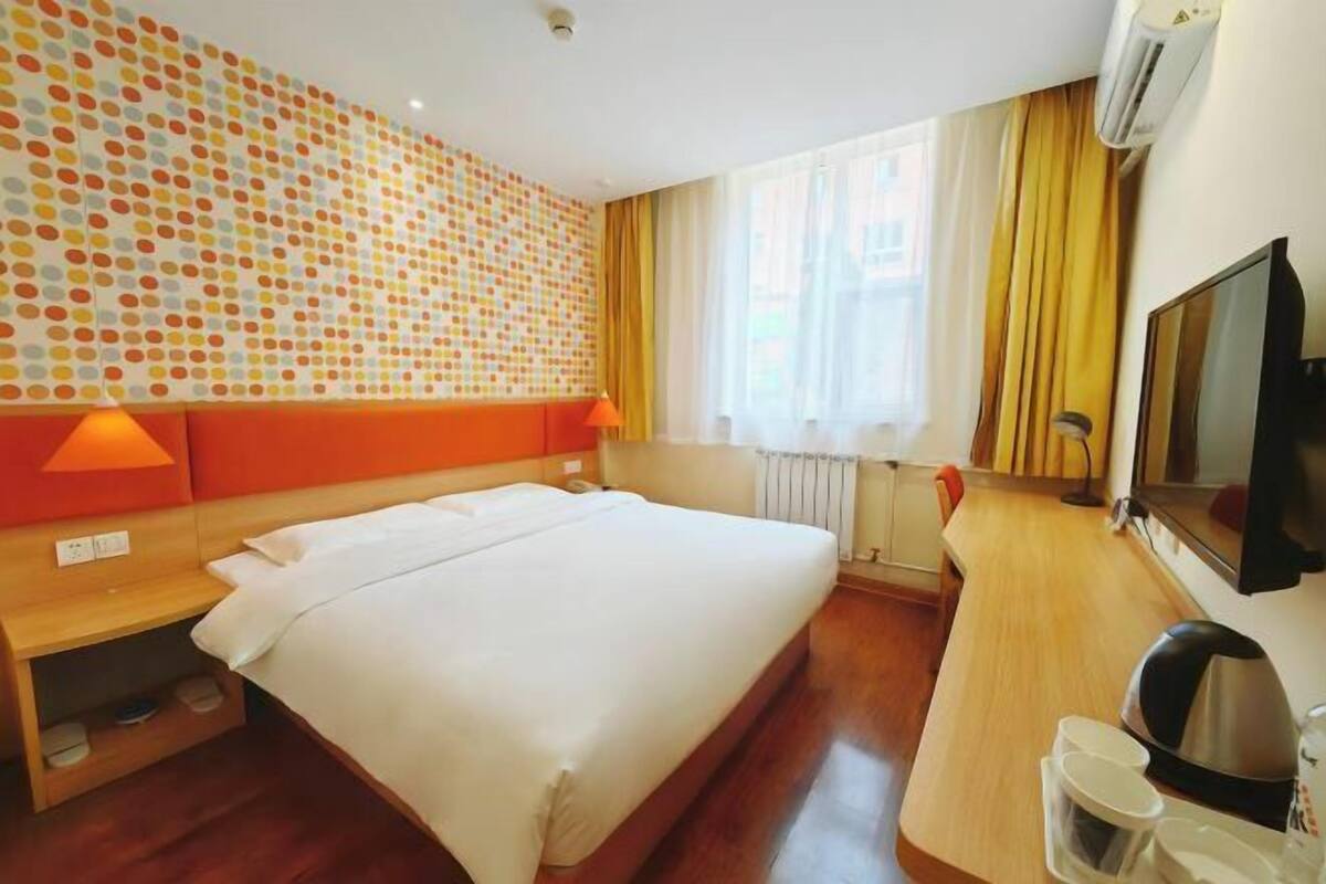 Una habitación de hotel con cama, escritorio, televisión y una pared con estampado de lunares.