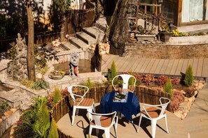 A patio with a round table and chairs, surrounded by plants and a stone wall. - Hengchangbao Garden Pinsu Lvyexianzongyulin Guanjing Inn (Lijiang)