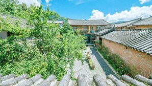 A traditional courtyard with tiled roofs, a stone pathway, and lush greenery. - Hengchangbao Garden Pinsu Lvyexianzongyulin Guanjing Inn (Lijiang)