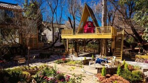 A wooden deck with a red play structure, surrounded by a garden with various plants and a traditional building in the background. - Hengchangbao Garden Pinsu Lvyexianzongyulin Guanjing Inn (Lijiang)
