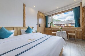 A hotel room with a large bed, a wooden headboard, a small table with a vase, and a view of traditional architecture outside the window. - Hengchangbao Garden Pinsu Lvyexianzongyulin Guanjing Inn (Lijiang)