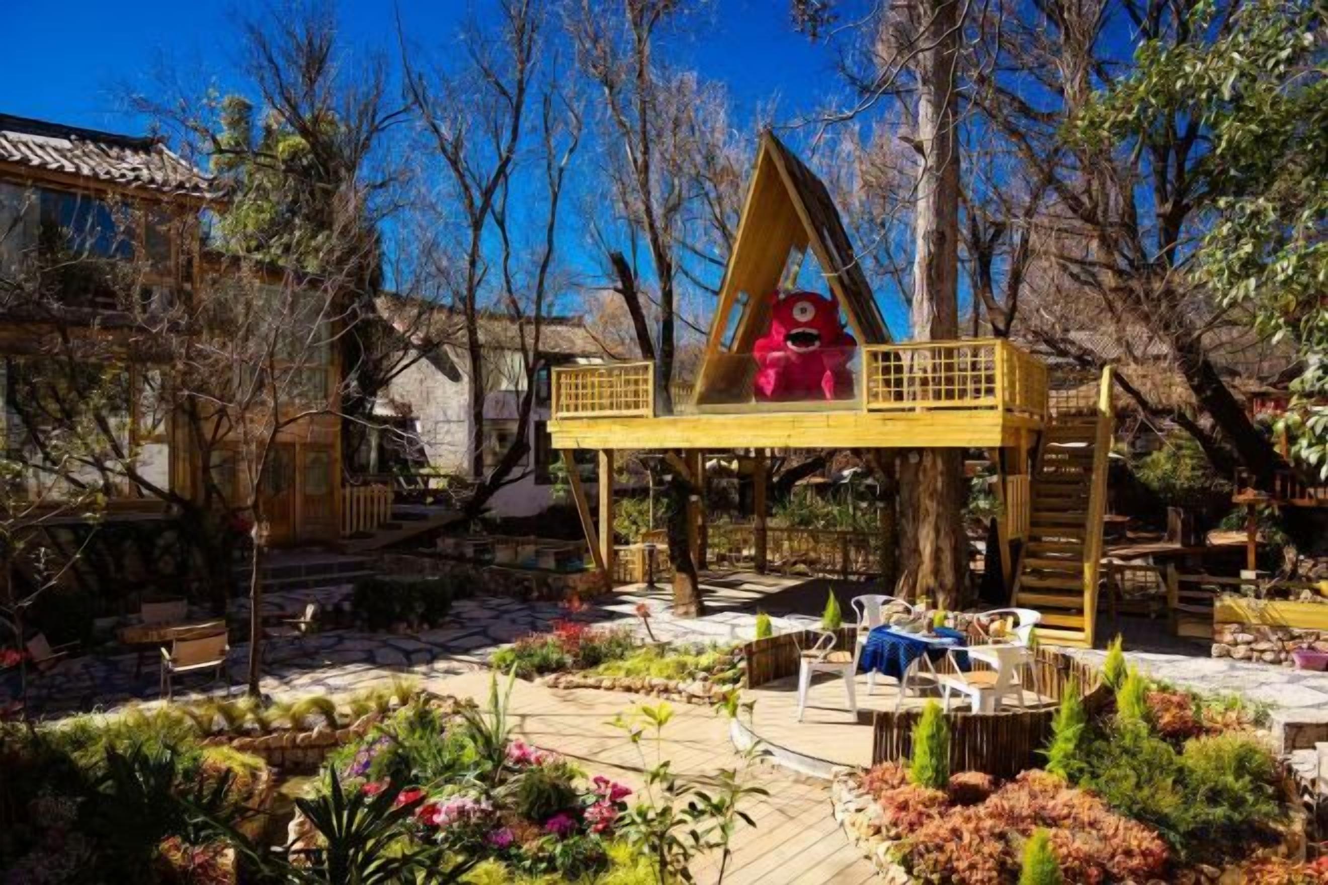 A traditional wooden structure with a triangular roof, surrounded by a garden with various plants and a wooden deck.