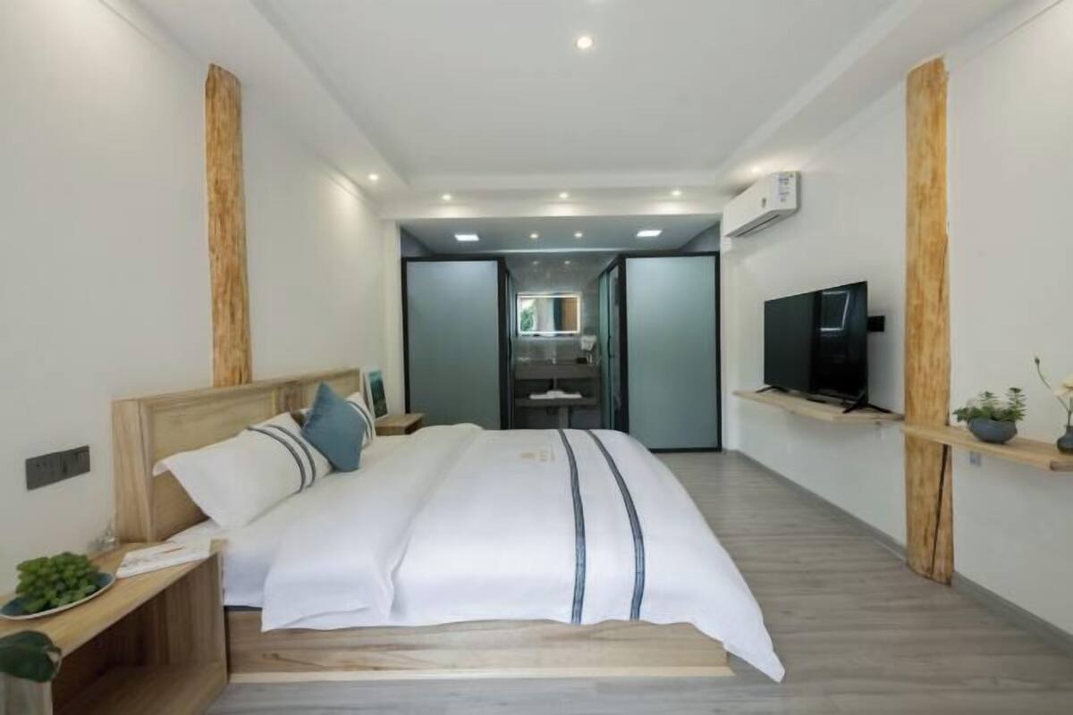 Ein modernes Hotelzimmer mit einem großen Bett, Holzelementen, einem Fernseher und einer kleinen Pflanze.