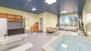 A modern living room with a large window, a sofa, a coffee table, and a kitchen area with cabinets and a refrigerator. - Yeongheungdo Sunset Spa Pension (Incheon)