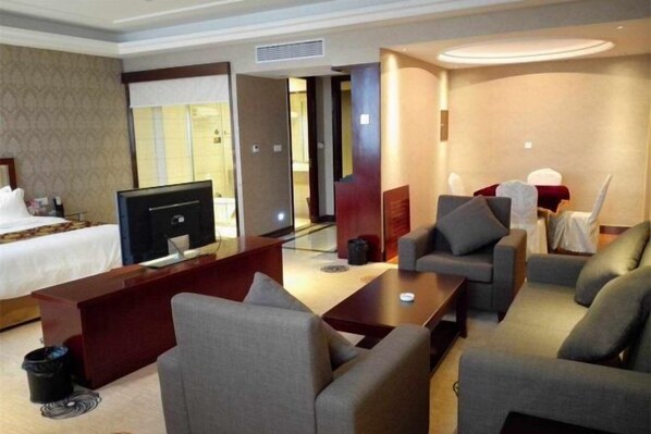 A hotel room with a bed, a desk with a computer, a TV, and a seating area with sofas. - Merlinwan Traders Hotel (Hangzhou)
