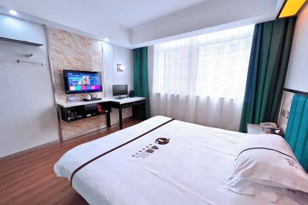 Habitació d'hotel amb un llit, un escriptori amb un ordinador, una televisió i una finestra amb cortines.