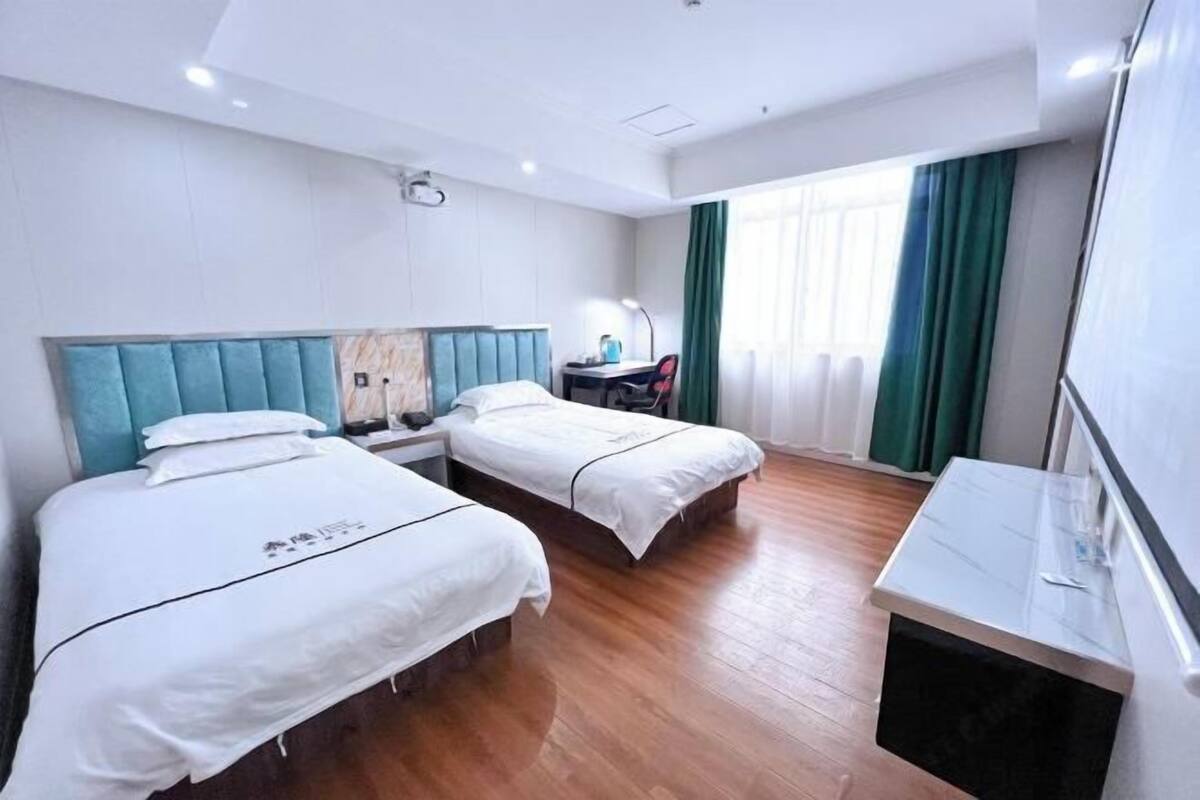 Habitació d'hotel amb dos llits, escriptori, cadira i finestra gran amb cortines.