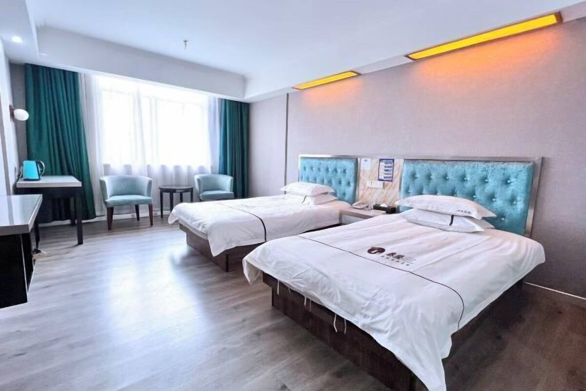 Habitació d'hotel amb dos llits, una taula de treball, cadires i una finestra amb cortines.