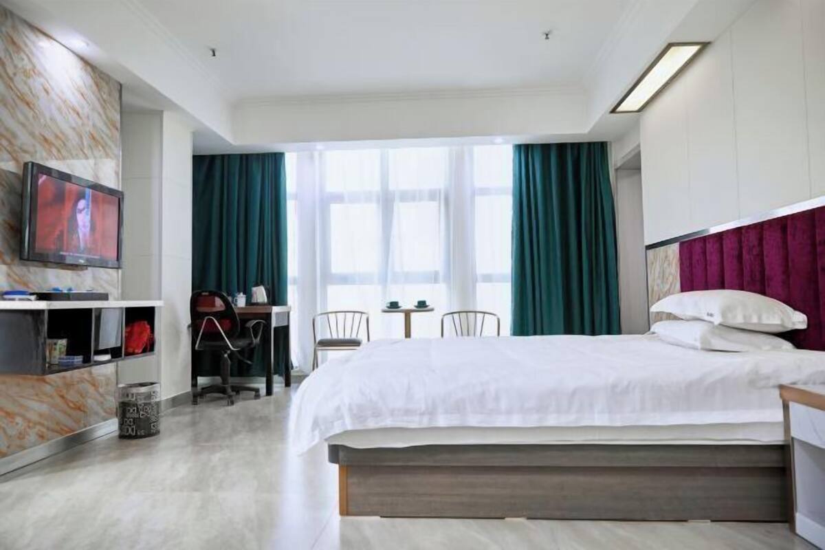 Habitació d'hotel amb llit, escriptori, cadira, televisió i finestra amb cortines.