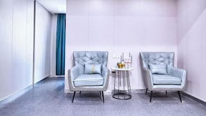 Een moderne hotelkamer met twee grijze gestoffeerde fauteuils, een klein rond tafeltje en een blauw gordijn.
