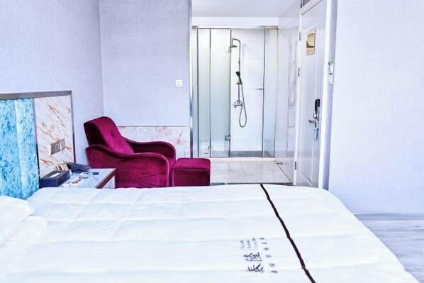 A hotel room with a bed, a red chair, and a shower area.