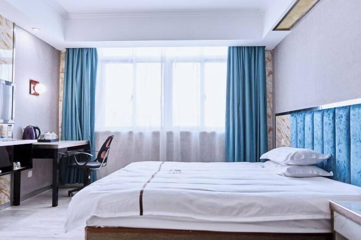 Habitació d'hotel amb un llit, un escriptori, una cadira i una finestra amb cortines.