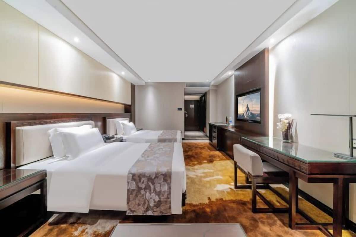Habitación de hotel con dos camas, un escritorio, una silla y un televisor.
