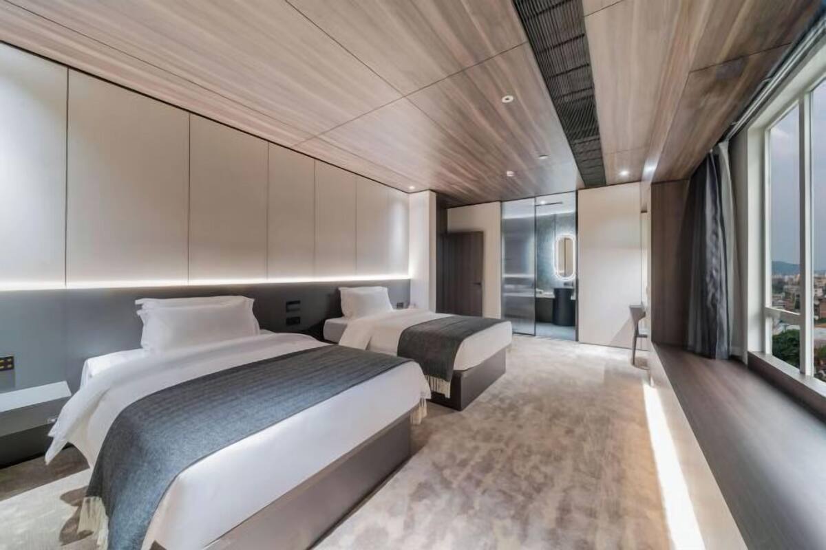 Habitación de hotel moderna con dos camas, un ventanal grande y vistas a la ciudad.