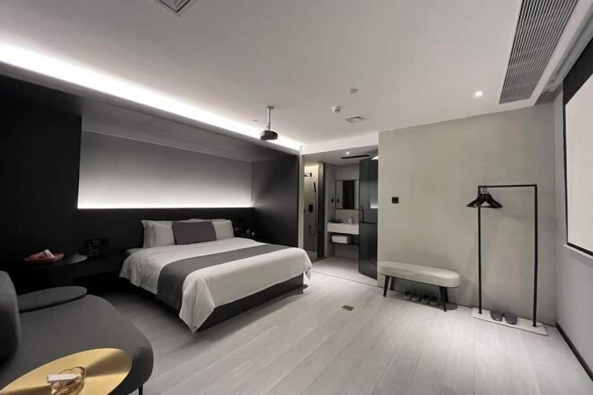 Una habitación de hotel moderna con una cama grande, mesitas de noche, un banco, un espejo y un zapatero.