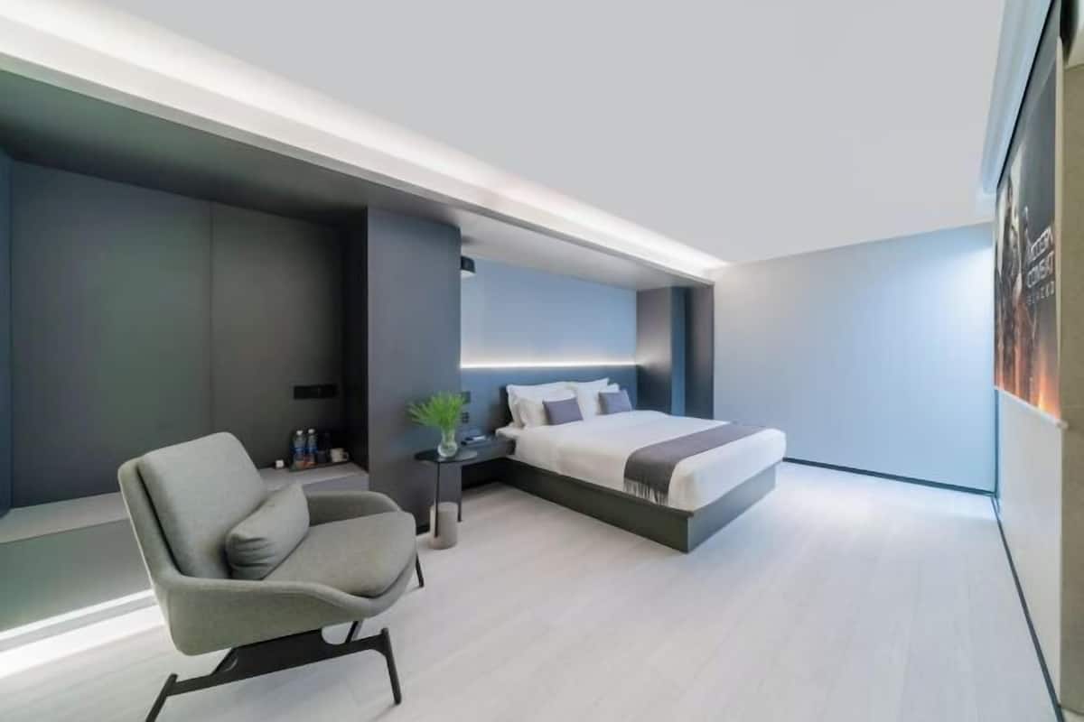 Un dormitorio moderno con una cama, una silla, una mesita de noche y un televisor montado en la pared.