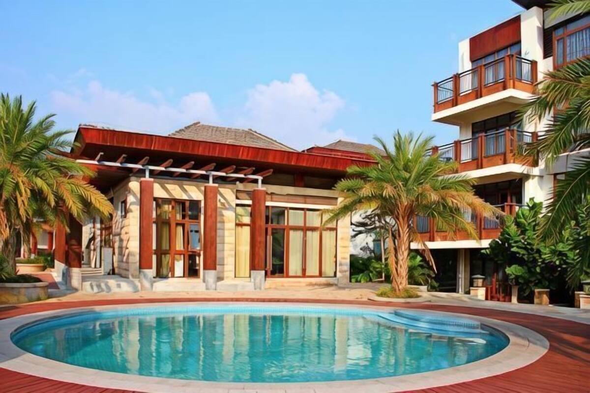 Un hôtel doté d’une piscine, de palmiers et d’un bâtiment au toit rouge.