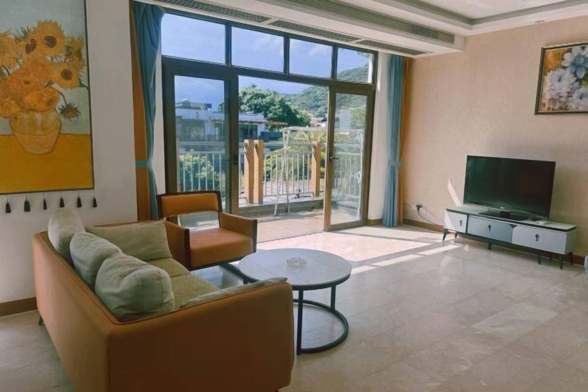 Un salon avec un canapé, une petite table, un téléviseur et un balcon offrant une vue agréable.