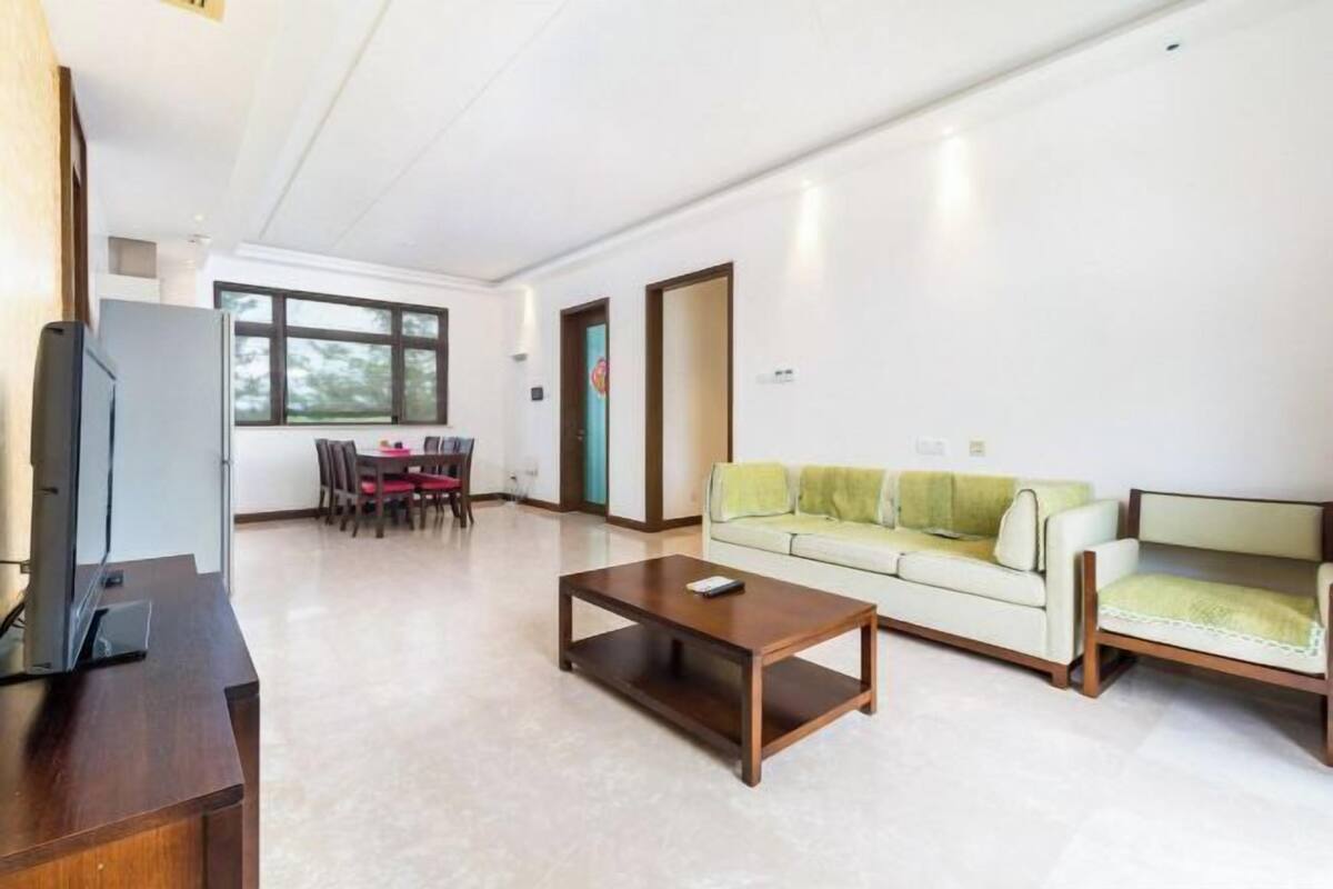Un salon avec un canapé, une table basse et un téléviseur. On aperçoit un coin repas au fond de la pièce.