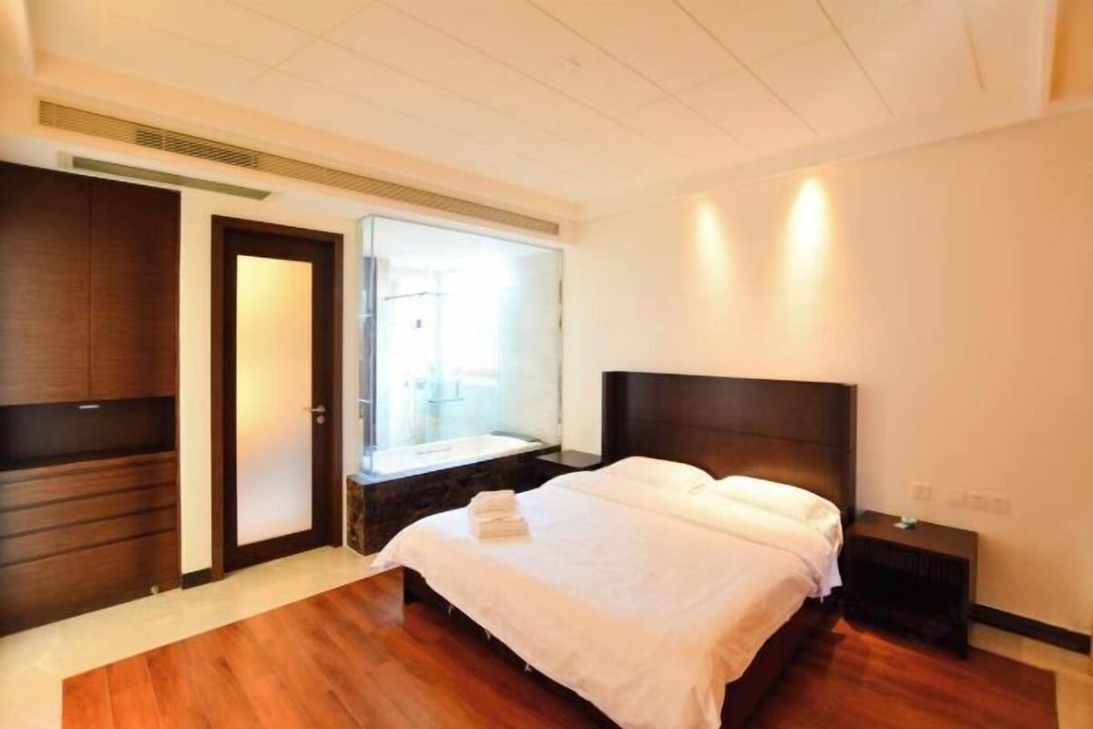 Une chambre à coucher comprenant un lit, une table de chevet, une armoire en bois, un miroir et une salle de bain avec un lavabo et une douche.