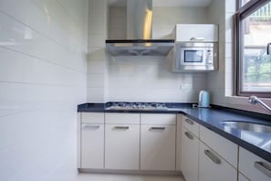 A modern kitchen with white cabinets, a black countertop, a stainless steel sink, a microwave, and a window. - Sanya Xiyue Luxury Villa (Yalong Bay Forest Park Branch) (Sanya)