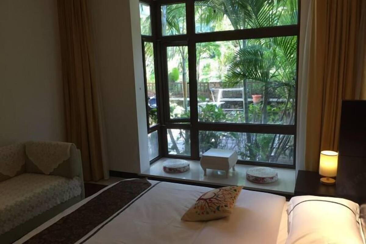Une chambre d’hôtel avec une grande fenêtre, un lit, un canapé et une table de chevet avec une lampe.