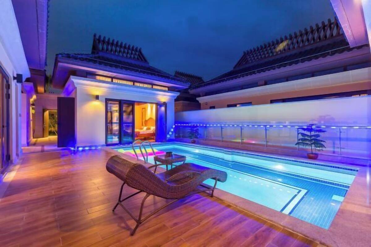 Une piscine avec des chaises longues, un bâtiment à l’architecture traditionnelle et un ciel étoilé.