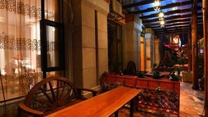 Un banco y una silla de madera en un espacio exterior bien iluminado, con suelo de piedra y plantas en macetas.