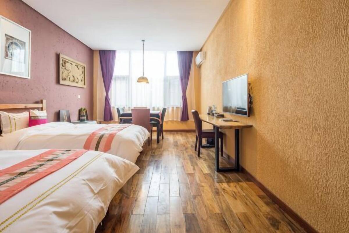 A hotel room with two beds, a desk with a chair, a television, and a large window with curtains.