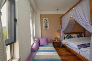 A bedroom with a bed, a sofa, a nightstand, and a window.