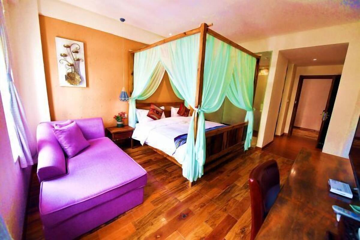 A room with a four-poster bed, a purple sofa, and a wooden dining table.