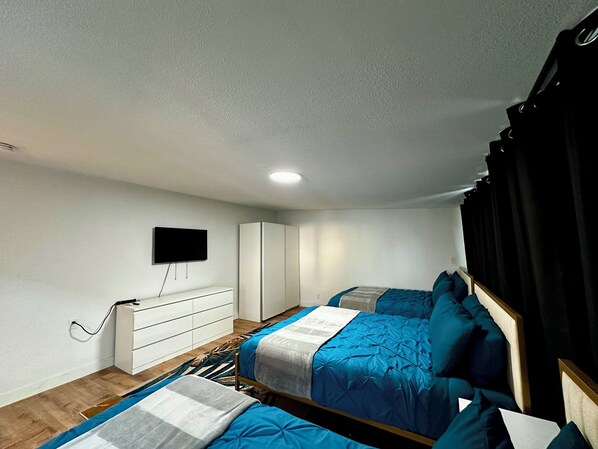 A bedroom with two beds, a TV mounted on the wall, a wardrobe, and a desk.
