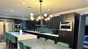 Une cuisine moderne avec des meubles de couleur sombre, des appareils en acier inoxydable, un îlot en marbre et un coin repas doté de chaises à revêtement vert.