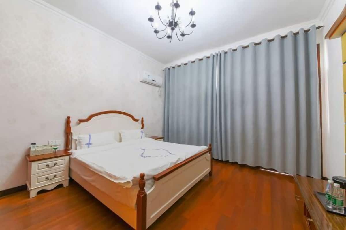 A bedroom with a wooden bed, a nightstand, a chandelier, and a window with curtains.