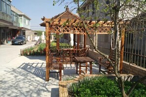 Un quiosco de madera con bancos, rodeado por un jardín con diversas plantas.