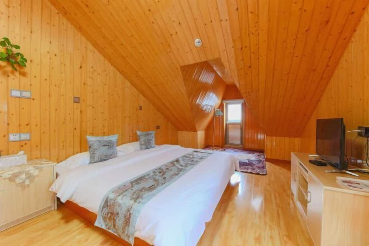 A bedroom with a wooden ceiling, a bed with white bedding, a television, and a small desk.