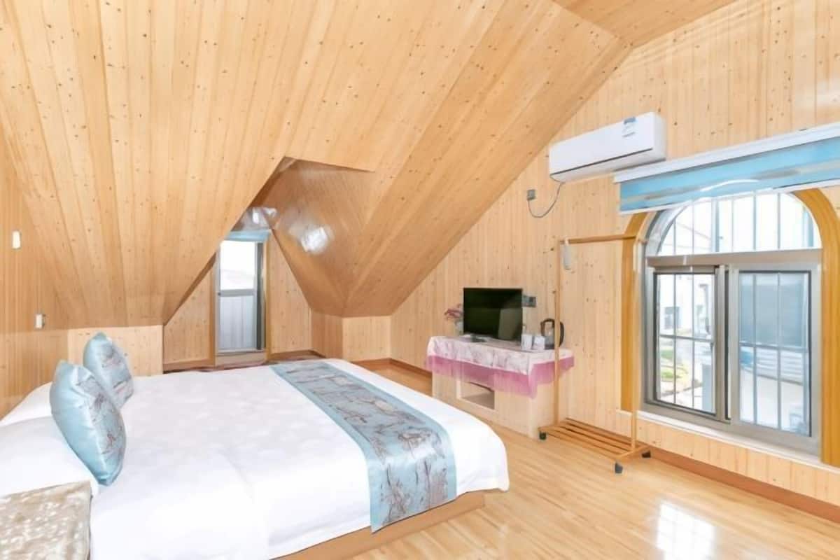 A bedroom with a wooden ceiling, a bed with pillows, a TV, a window, and an air conditioning unit.