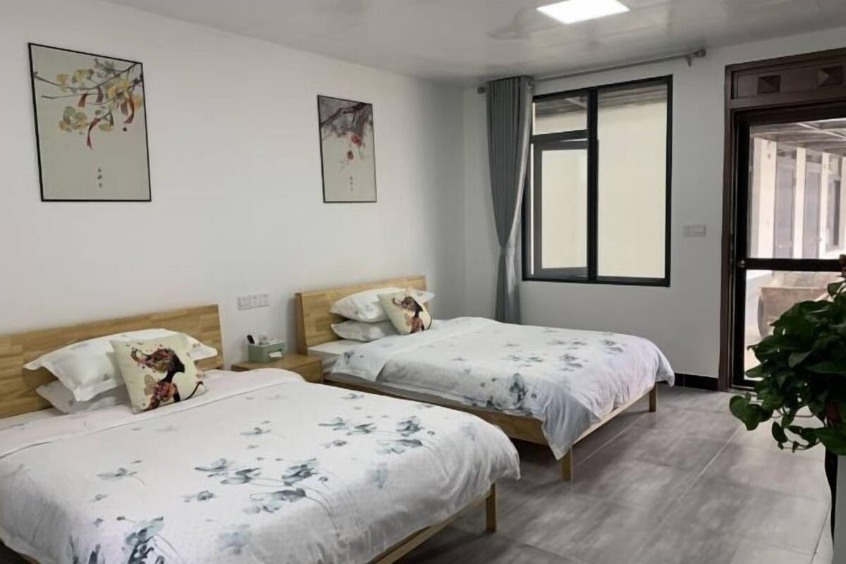 A hotel room with two beds, a window with curtains, and artwork on the walls.