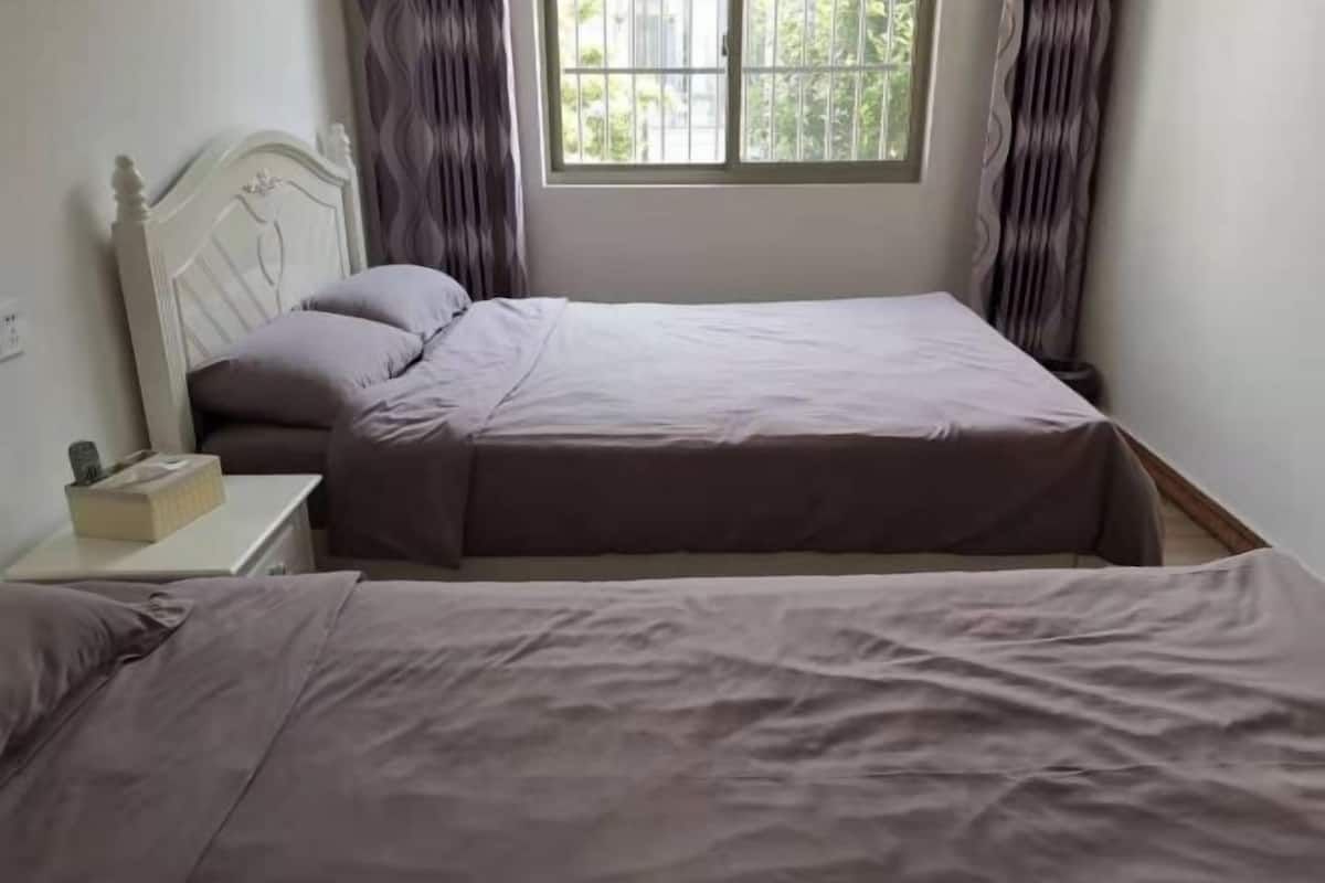 A single bed with a headboard, a bedside table with a tissue box, and a window with curtains.