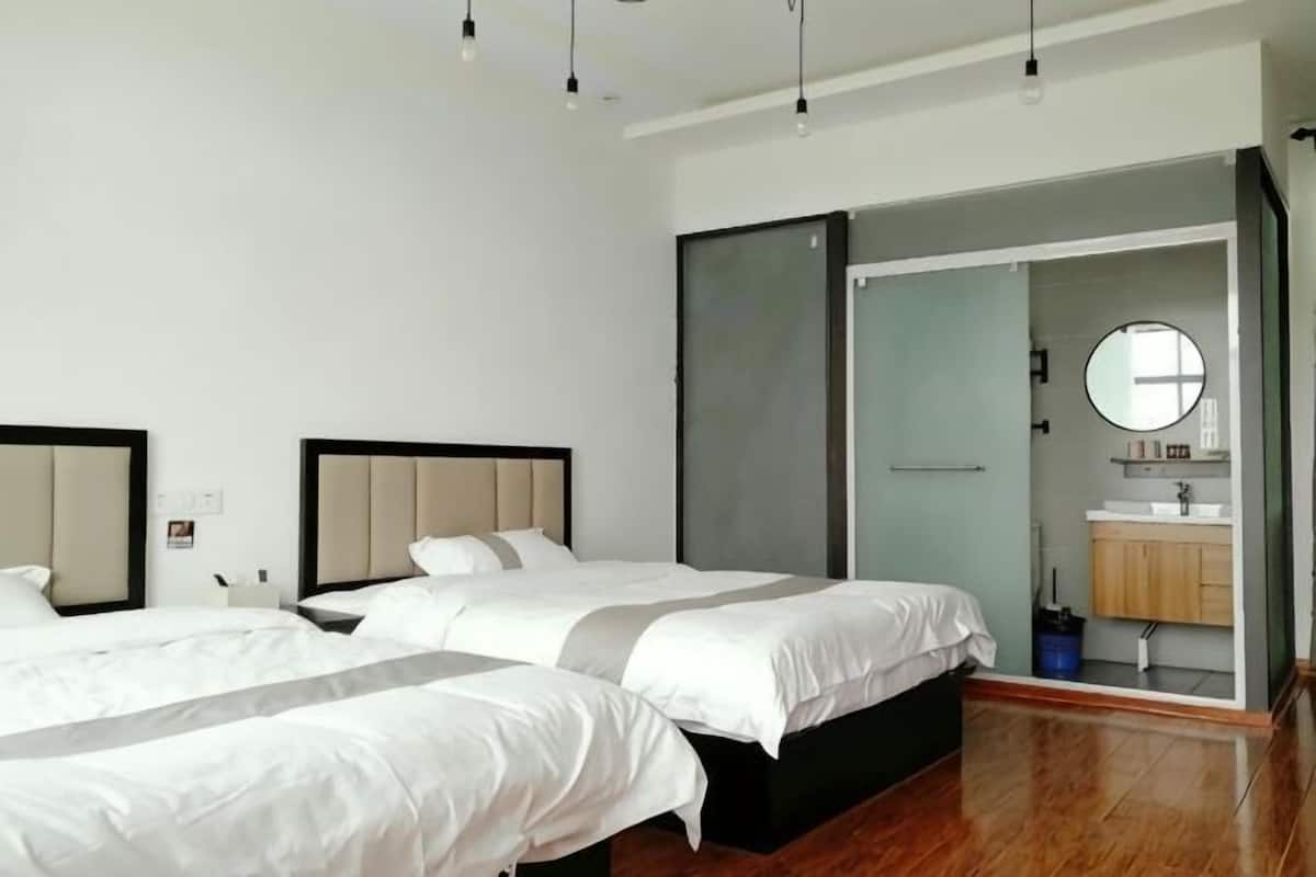 A modern hotel room with three beds, a sliding door to a bathroom, and a large mirror.