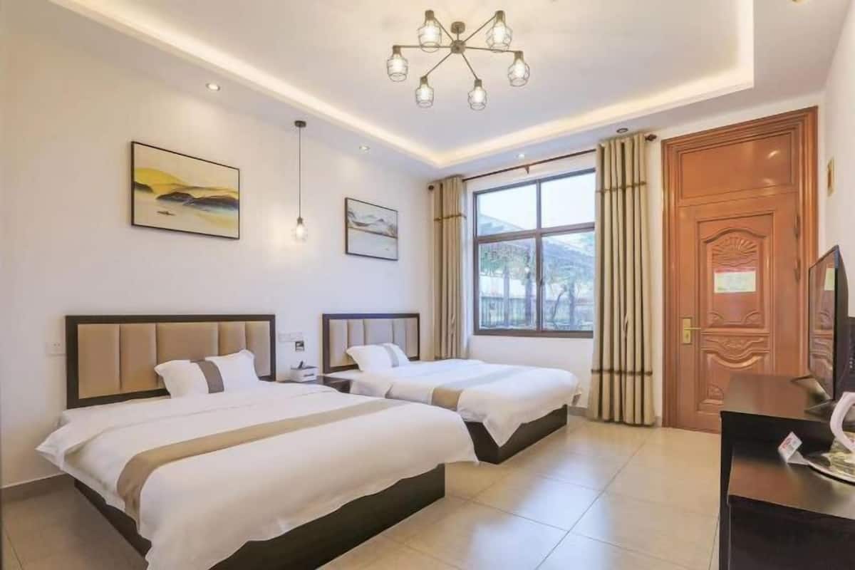 A hotel room with two beds, a large window with a view, a wooden door, and a desk with a chair.
