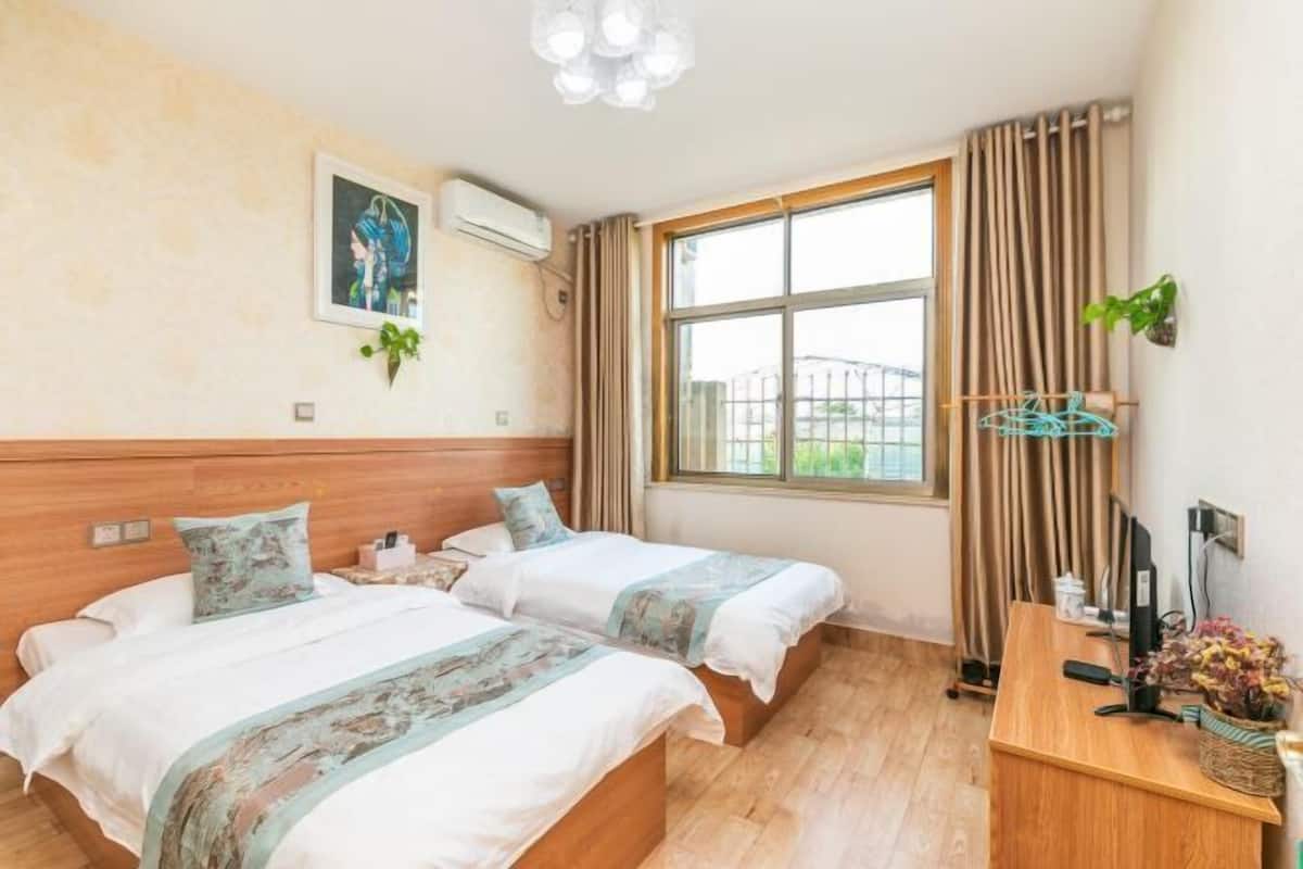 A hotel room with two beds, a desk, a window with curtains, and a painting on the wall.