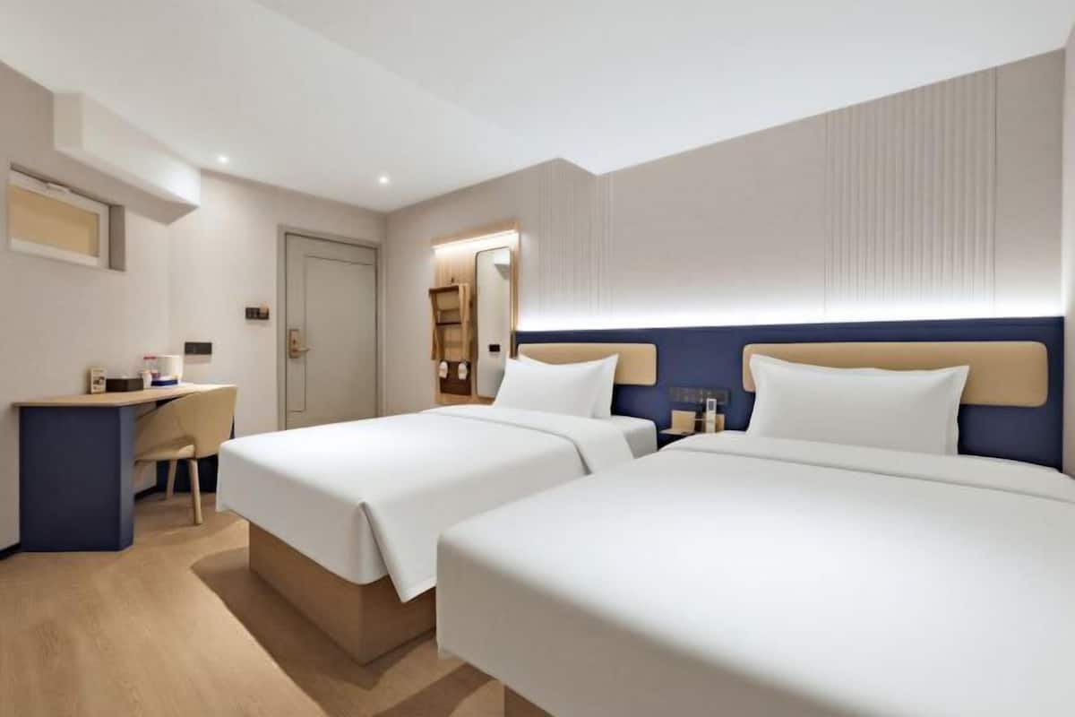 A hotel room with two beds, a desk, and a mirror.