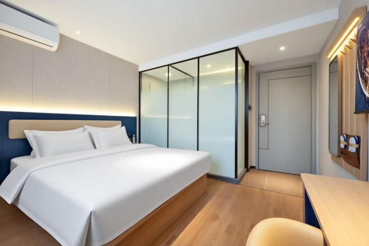A modern hotel room with a large bed, a desk, and a sliding glass door closet.