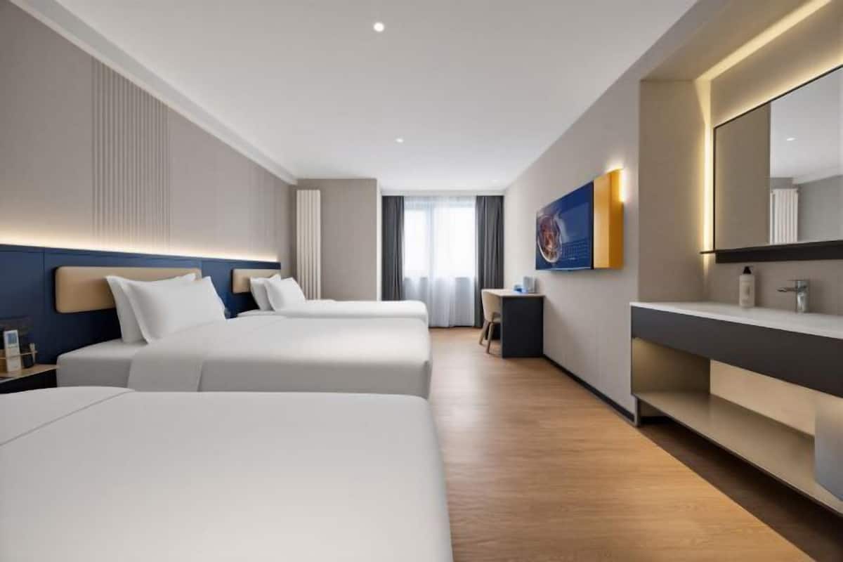 A modern hotel room with two beds, a desk, a large mirror, and a view of the city.