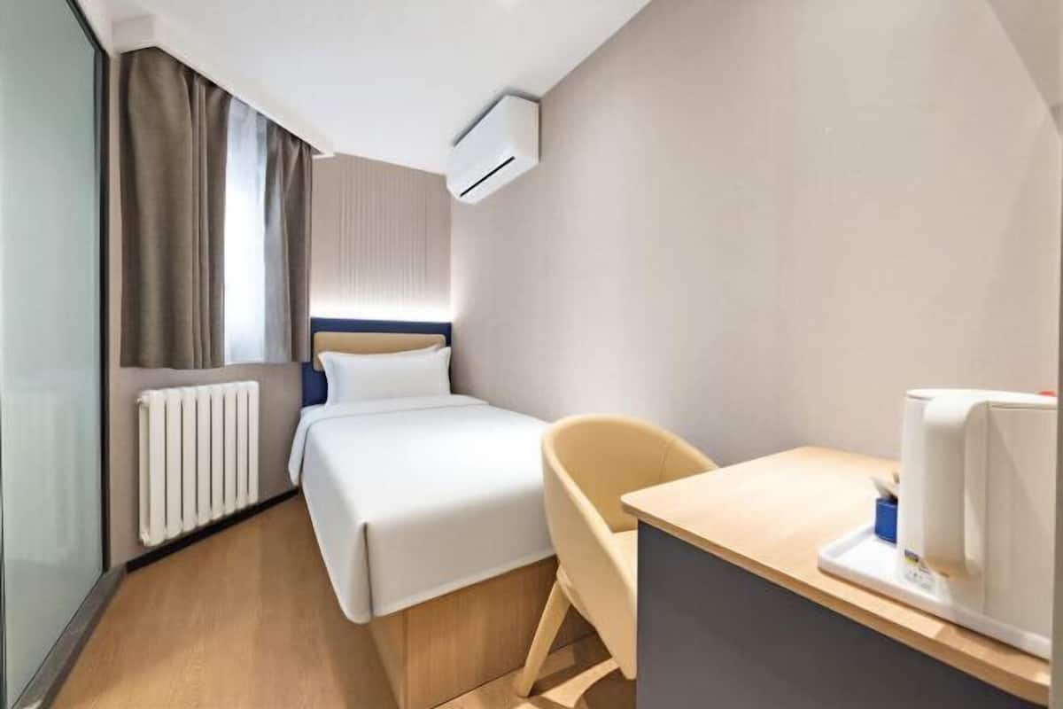 A hotel room with a bed, a chair, a desk, an air conditioner, and a radiator.