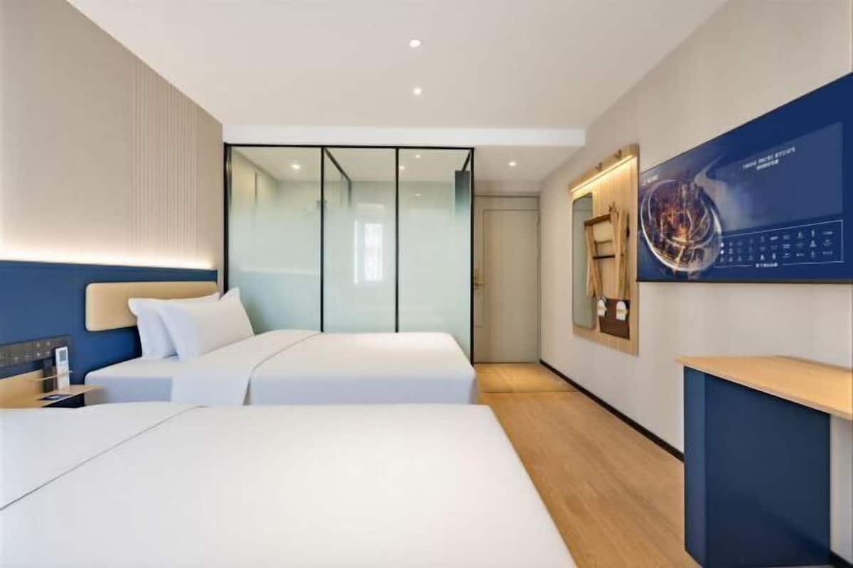 A modern hotel room with two beds, a glass partition, a wooden floor, and a large poster on the wall.