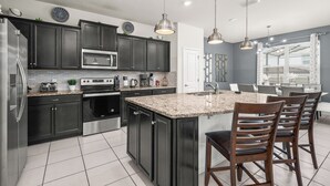 Una cocina moderna con armarios oscuros, electrodomésticos de acero inoxidable, encimera de granito e iluminación colgante.