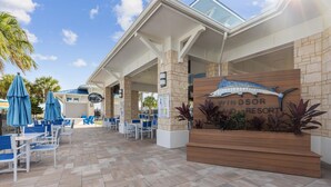 Un área de estar al aire libre en un resort, con mesas y sillas, una jardinera de madera con plantas y un letrero que indica Windsor Resort.